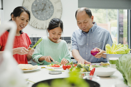 Little girl is helping to prepare vegatables with her grandparents. They are making a stir fry for dinner. の写真素材