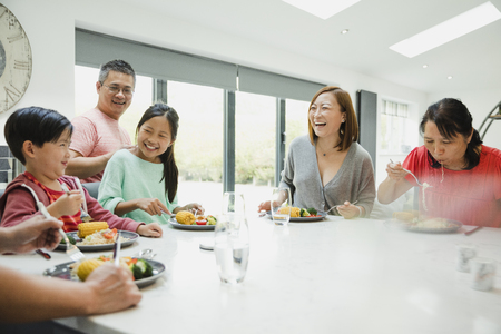 Family are eating a stir fry together in the kitchen of their home. Everyone is looking at the little boy who is making a silly face. の写真素材