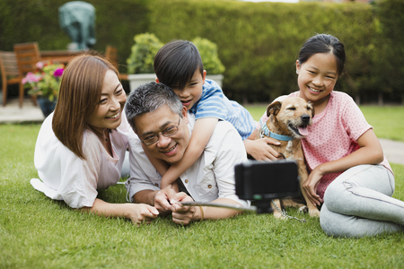 Family are taking a selfie with a smartphone on a selfie stick in their garden with their pet dog. の写真素材