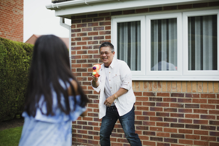 Little girl is having a water fight in the garden with her dad using water pistols.の写真素材