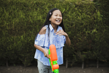 Little girl is having a water fight in the garden with her family. She is laughing with a water pistol in her hand.の写真素材