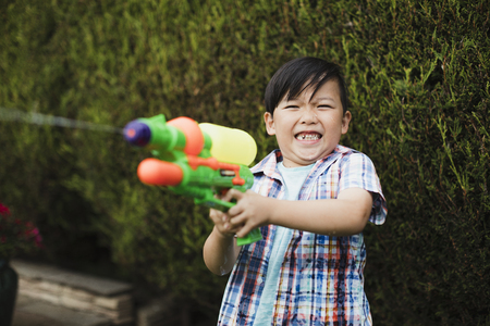 Little boy is having a water fight in the garden with his family. He is making a face as he gets hit with a water pistol in his hand.の写真素材