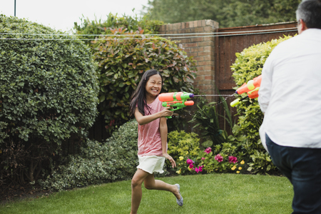 Little girl is having a water fight in the garden with her dad using water pistols.の写真素材