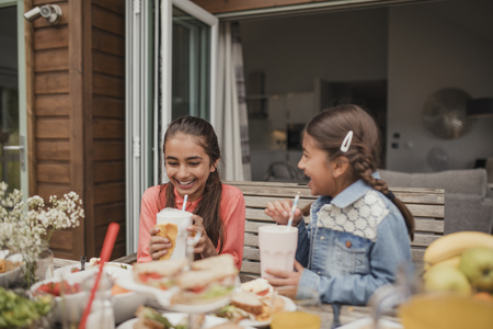 Two little girls enjoying milkshakes outside holiday cottage.の写真素材