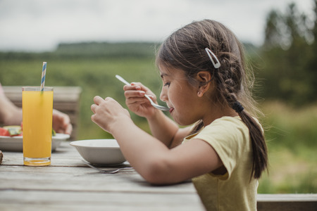 Side view of little girl eating cereal outside in summer while on holdiay.の写真素材
