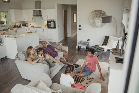 Family relaxing in their holiday home. Two of the children are playing chess while the rest of the family watch.の写真素材