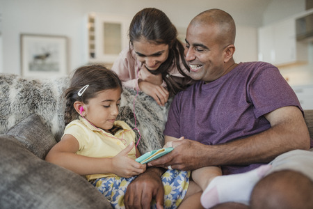 Father and his two daughters using and looking at the digital tablet and laughing.の写真素材
