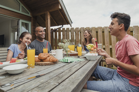 Family sitting outside holdiay lodge and eating breakfast.の写真素材