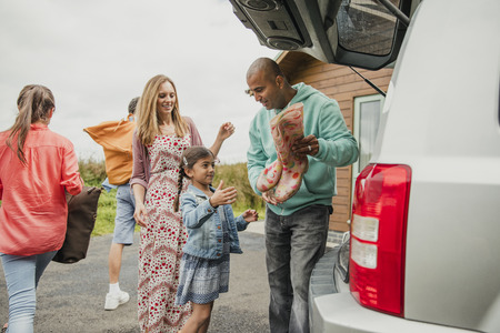 Little girl and mother helping her father unpack the car at holiday cottage.の写真素材
