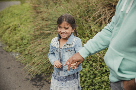 Little girl standing outside, laughing and holding her fathers hand.の写真素材