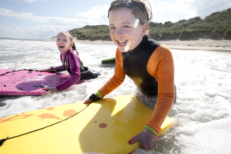 Two little girls are smiling for the camera while bodyboarding in the sea.の写真素材