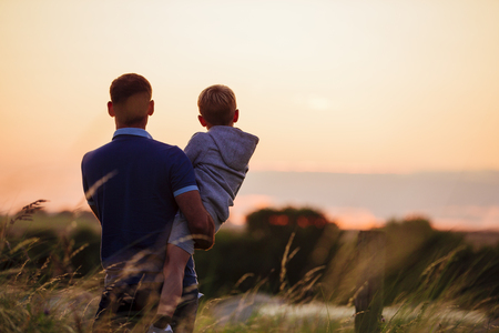 Father and son watching the sun set over the beach while stood on the sand dunes.の写真素材