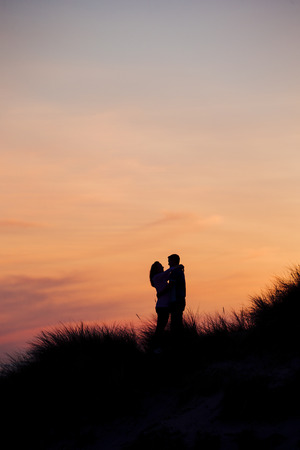 Silhouette of a couple standing, holding each other, on a sand dune during a sunset.の写真素材