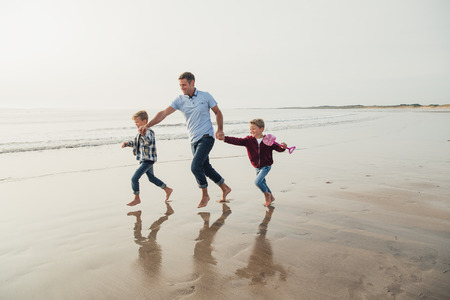 Father and two children having fun, laughing and smiling while running along the sea front.の写真素材