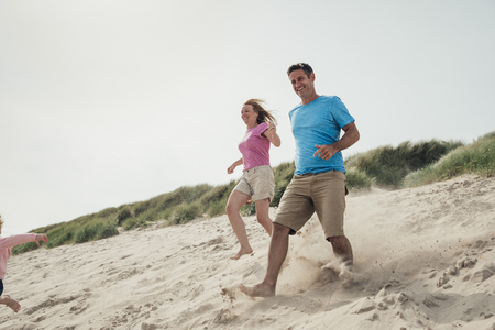 Low angle view of couple racing down a sand dune while on holiday at the seaside.の写真素材