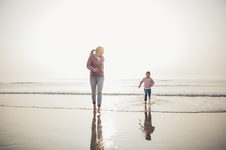 Wide angle view of mother and her daughter running from the tide coming in at the beach.の写真素材