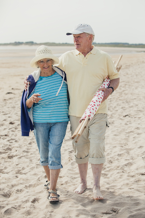 Elderly couple walking along the beach, arm in arm, on holiday.の写真素材