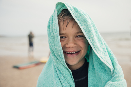 Little boy wrapped in a towel after surfing at the beach.の写真素材