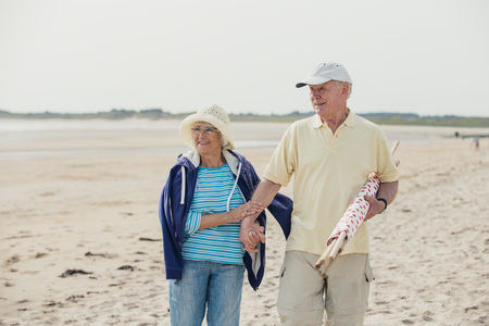 Elderly couple walking along the beach, arm in arm, on holiday.の写真素材