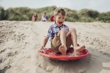 Young boy sliding down a sand dune while his family wait at the top.の写真素材