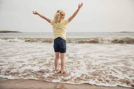 Little girl being free at the beach with her hands up in the air.