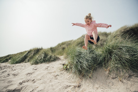 Little girl jumping over a sand dune while on holiday with her family, having some fun.の写真素材