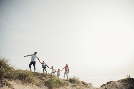 Family walking hand in hand along the top of a sand dune. Exploring the beach together.の写真素材