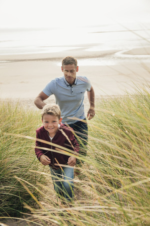 Father and son walking up a sand dune at the beach while on their vacation.の写真素材