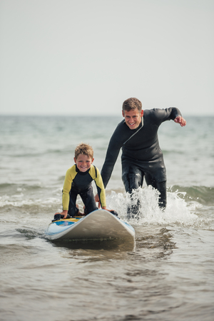 Little boy getting shown how to surf at the beach with his father.の写真素材