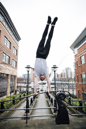 Teenage freerunner is doing a handstand on bridge railings in the city.の写真素材