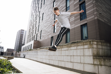 Young freerunner is jumping down from a wall in the city. の写真素材