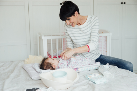 Baby has had her nappy changed by her mother on the double bed. The mother is fastening the baby grow while being playful.の写真素材