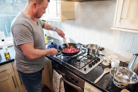 Mature man is making a spagetti bolognese at home. He is browning off the mince in a wok with onions.の写真素材