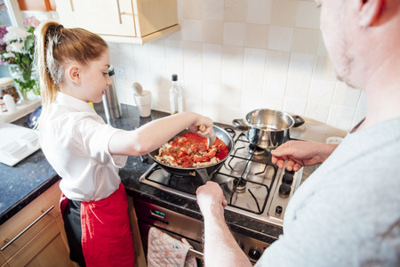 Little girl is learning how to cook with her father at home. They are making a spagetti bolognese together.の写真素材