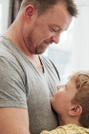 Little boy and his father are making eye contact while having a cuddle at home. の写真素材