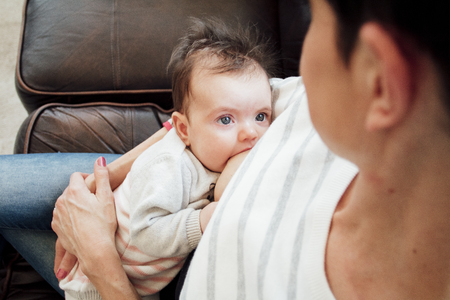 Newborn baby girl is looking at her mother while she breastfeeds her.の写真素材