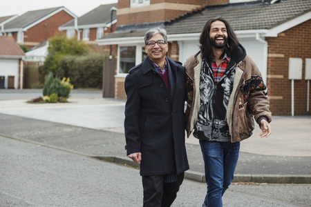Mid adult man and his mature father are laughing as they walk down the street together.の写真素材