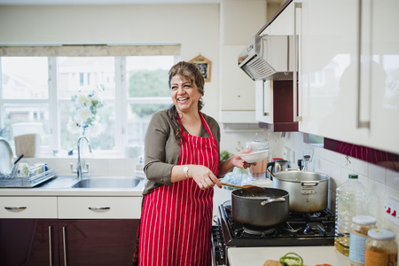 Mature woman is talking and laughing with someone out of the frame while she makes dinner at the cooker. の写真素材