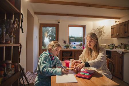 Mother and daughter sitting at the table in the morning. Mother is helping her daughter with her homework before school.の写真素材