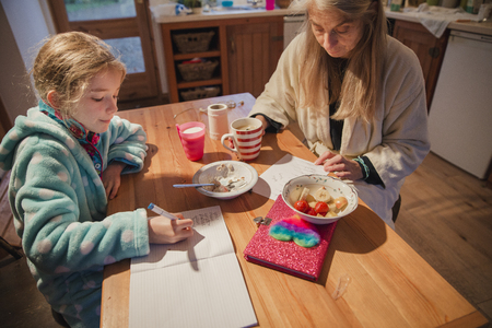 Mother and daughter sitting at the table in the kitchen. Mother is checking over her daughters homework before school.の写真素材