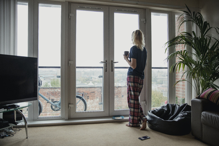 Rear view of a young female adult looking out the window after having her breakfast.の写真素材