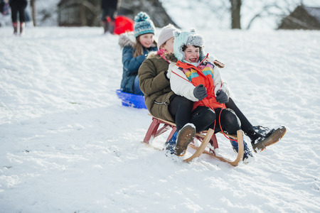 Children are having a race down a hill on different types of sleds.