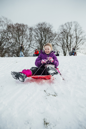 Low angle view of a little girl sledding down a hill in the snow.の写真素材
