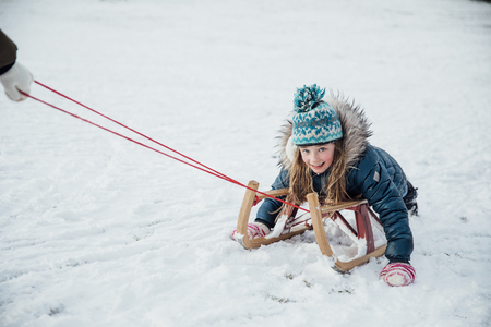 Little girl is smiling for the camera while being pulled on a sleigh in the snow.の写真素材
