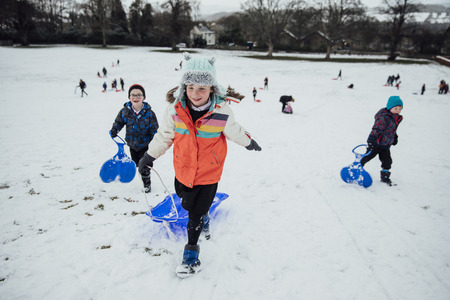 Children from the community are running up a hill to have a race together on sleds in the snow.