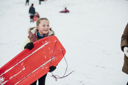 Little girl is socialising with her friends in the snow. She is talking while carrying a sled.の写真素材