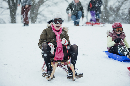 Little girl is going down a big snowy hill on a sleigh while wearing ski goggles.の写真素材