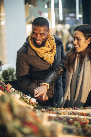 Front view of a couple standing at a christmas market stall deciding on what wreath they should buy.の写真素材