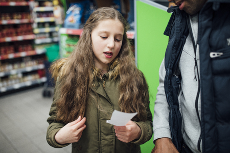 Little girl is reading things from a shopping list to her father in the supermarket.の写真素材