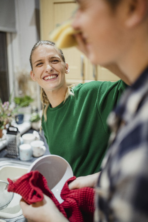 Young couple are washing and drying dishes at home. The girl is being playful and wiping her partner's face with the kitchen sponge.の写真素材